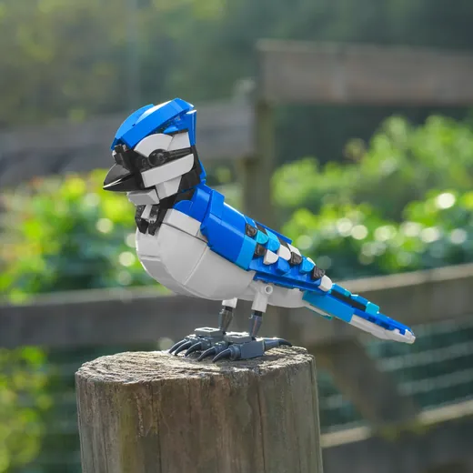A bluejay built from bricks, photographed outdoors on a fence post