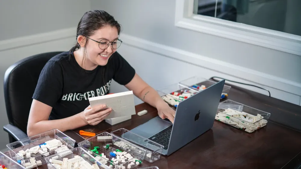 A Bricker Builds designer at her workstation with trays of brick elements and a laptop