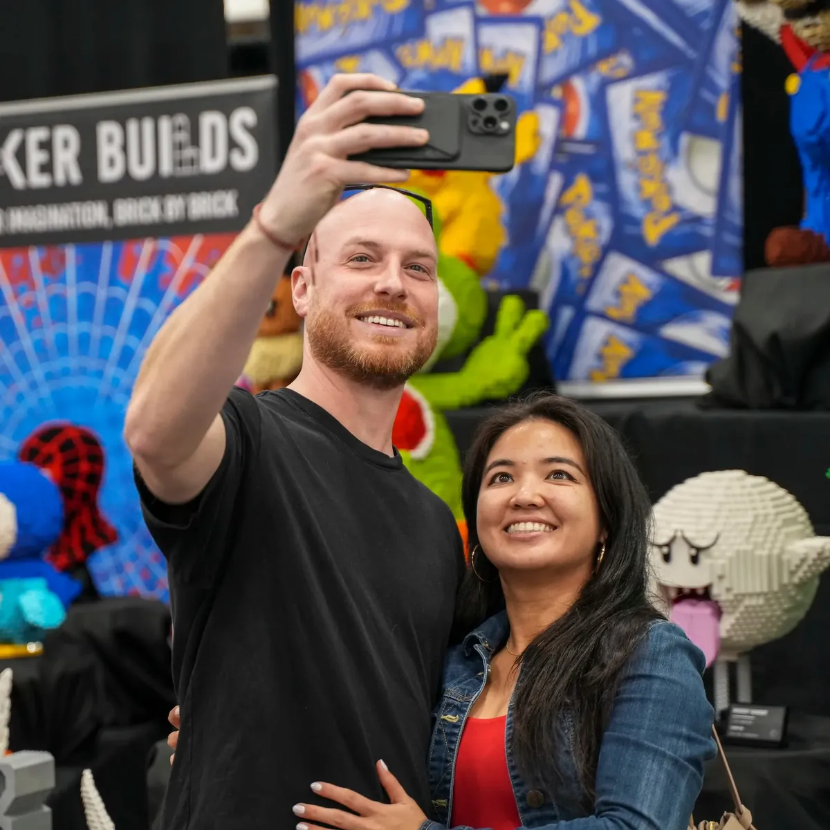 Two people taking a selfie with brick builds at a Bricker Builds convention booth